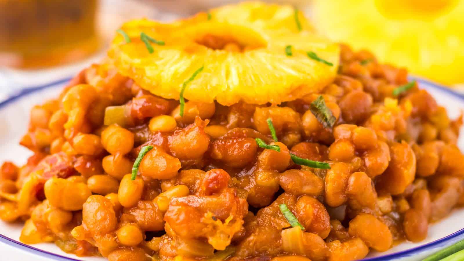 A plate of Hawaiian baked beans garnished with a pineapple slice and chopped herbs.