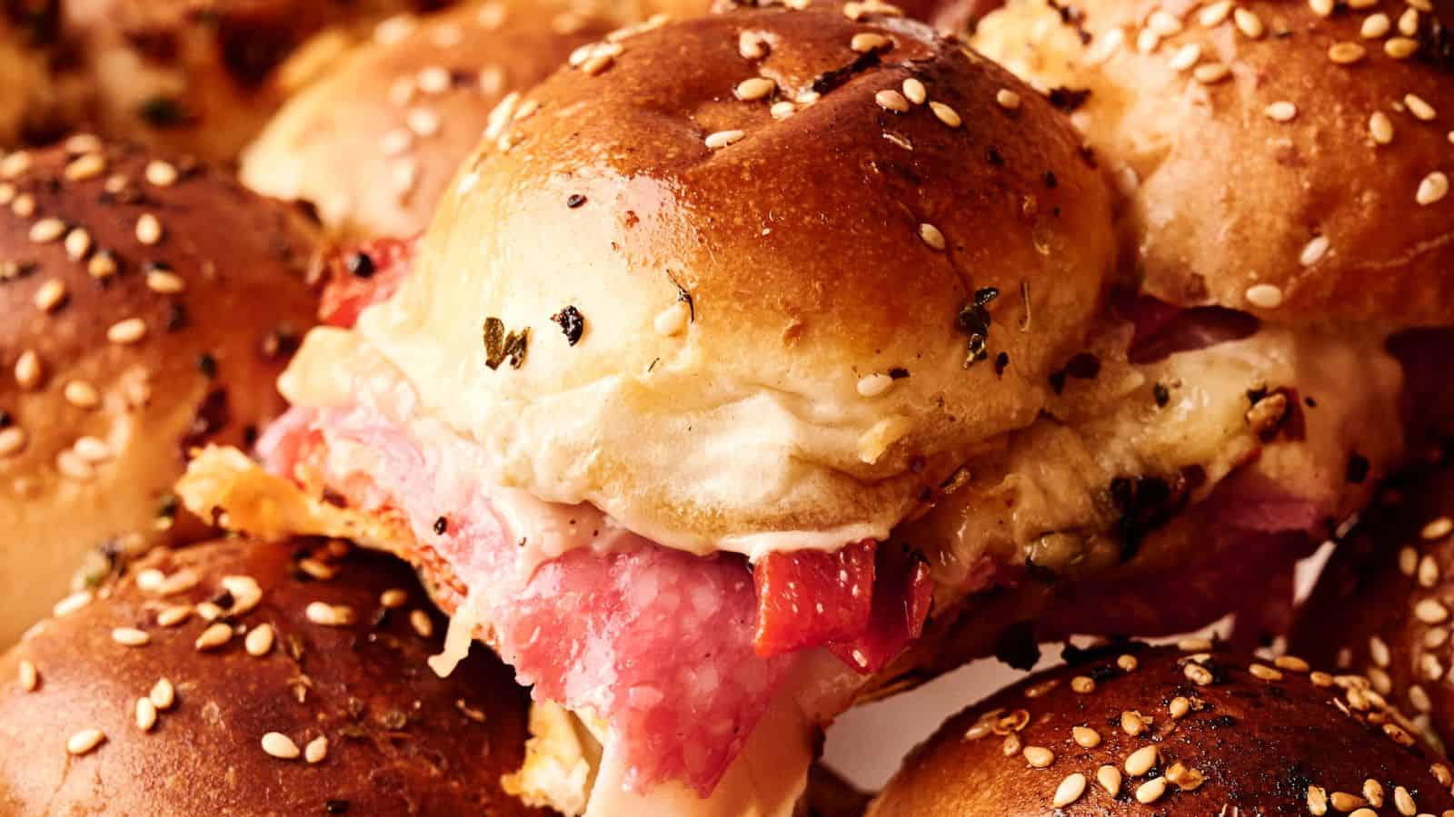 Close-up of sesame seed-topped sliders filled with sliced meat and melted cheese.