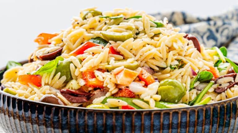 A bowl of orzo pasta salad with sliced olives, red peppers, spinach, and herbs.