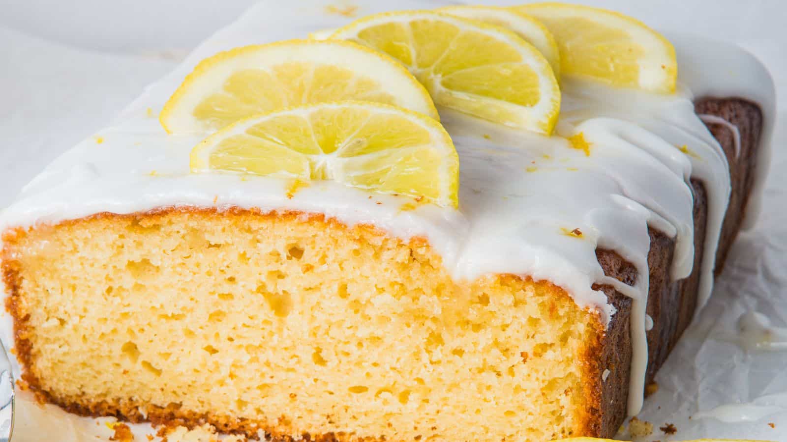 A sliced lemon cake topped with white icing and lemon slices.