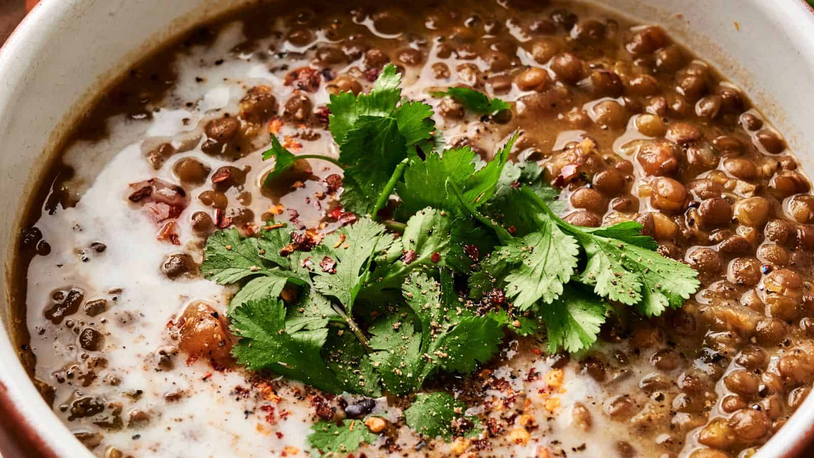 A hearty bowl of savory lentil soup, beautifully garnished with fresh cilantro, a swirl of cream, and an aromatic blend of spices.