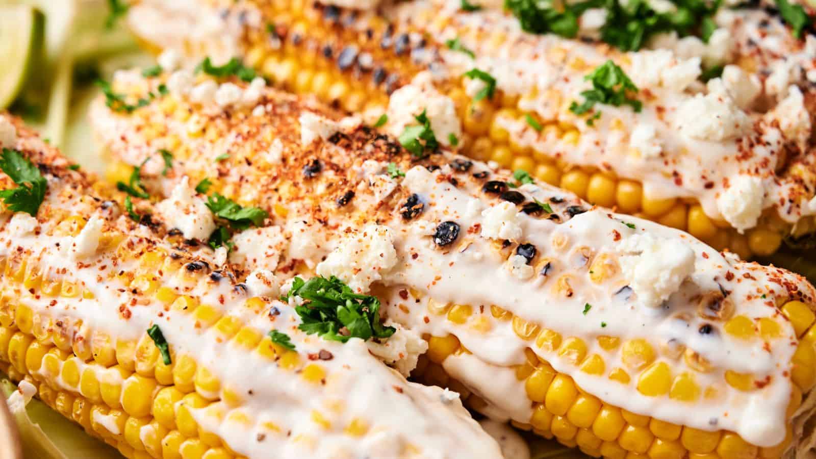 Close-up of Mexican Street Corn on the cob topped with creamy sauce, crumbled cheese, chili powder, and chopped cilantro.