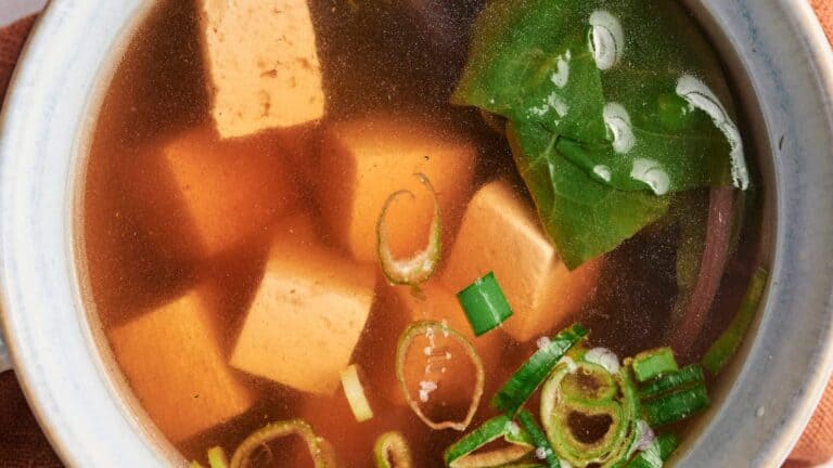 Miso Soup with tofu cubes, seaweed, and green onions on a bowl.