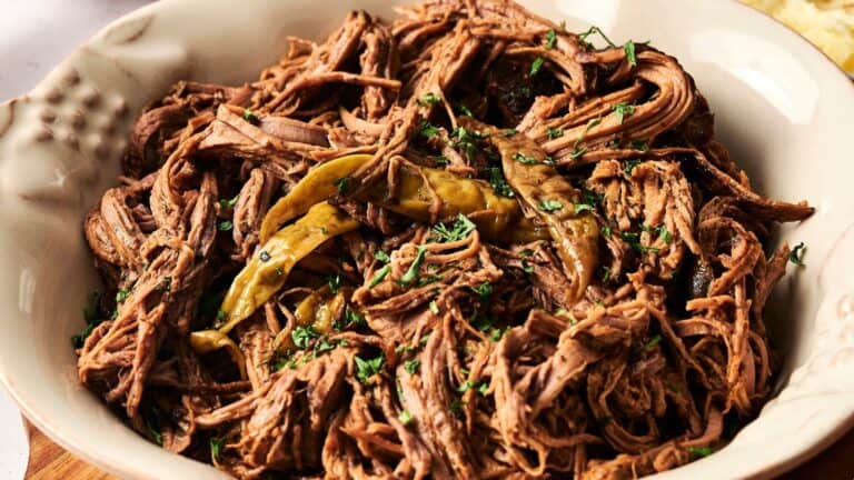 A plate of shredded beef garnished with green chili peppers and herbs.