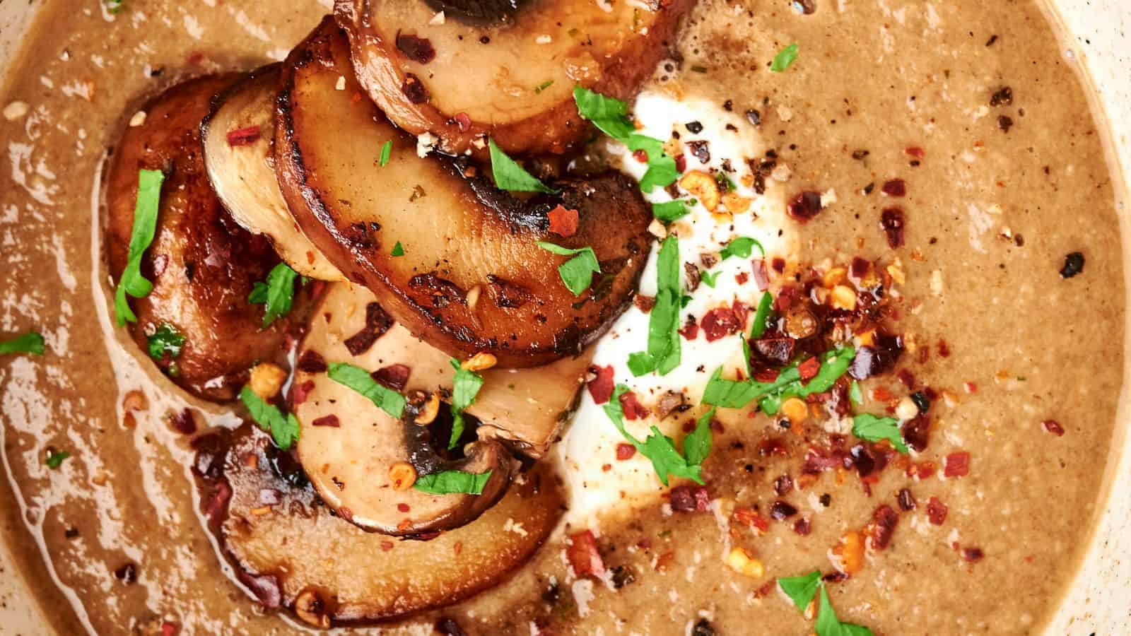 Mushroom soup that's delightfully creamy, adorned with sautéed mushrooms, a dollop of cream, red pepper flakes, and a sprinkle of parsley.