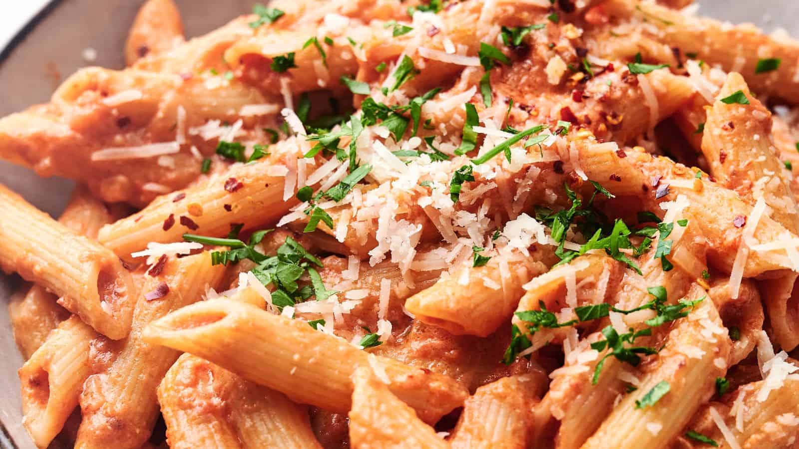 Two bowls of penne alla vodka, with Parmesan by the side.