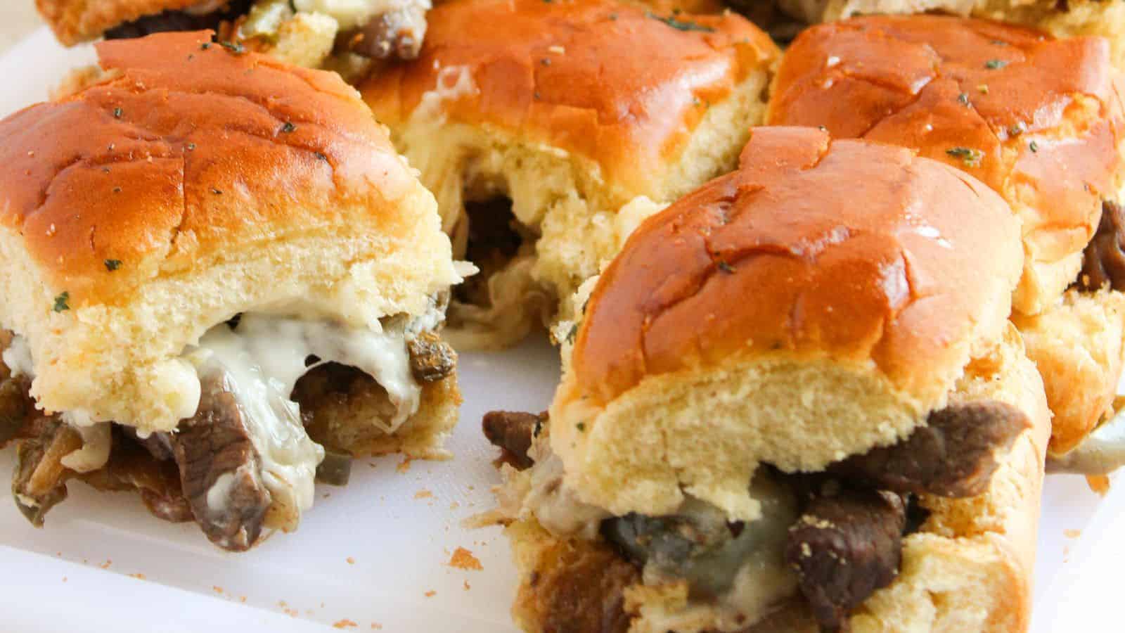 Close-up of beef and cheese sliders with toasted buns on a white surface.