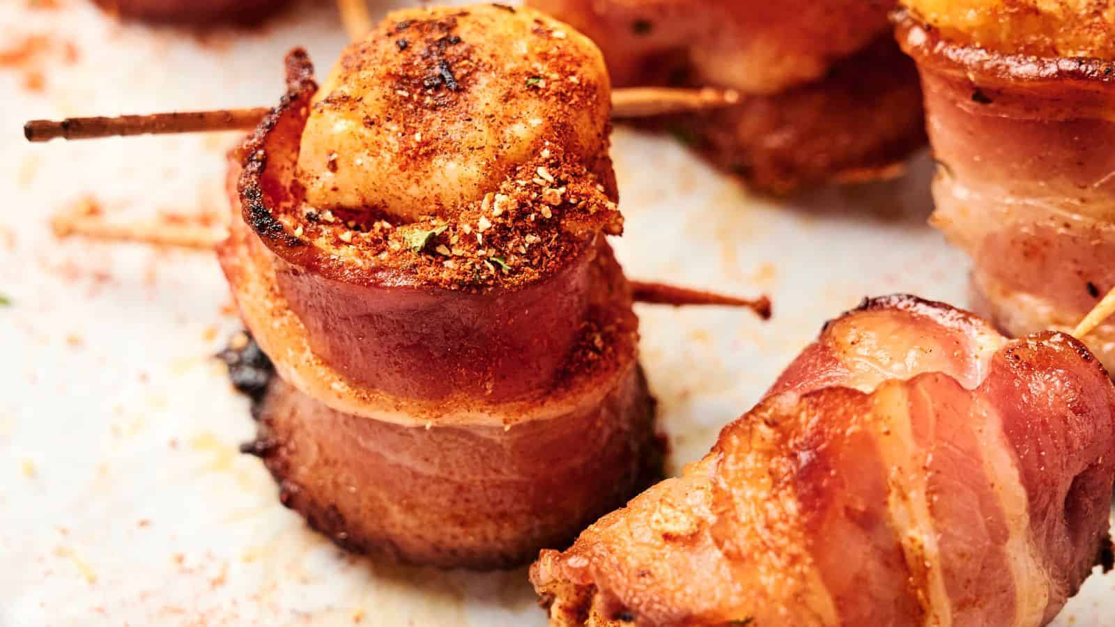 Close-up of bacon-wrapped scallops secured with toothpicks, seasoned with spices, and cooked until golden and crispy.