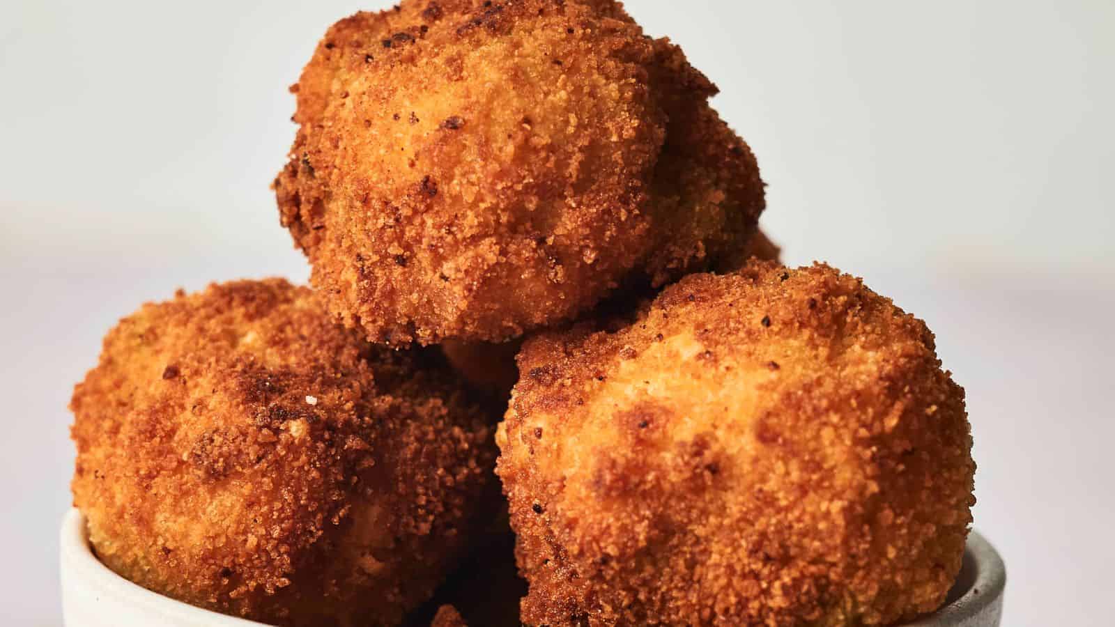 A bowl of golden-brown, crispy fried arancini served in a white dish on a plain background.