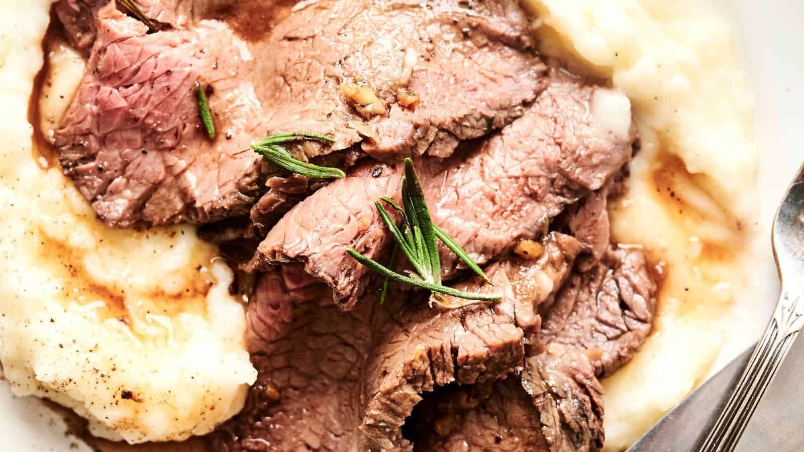 Sliced roast beef served on a bed of mashed potatoes, garnished with fresh rosemary.