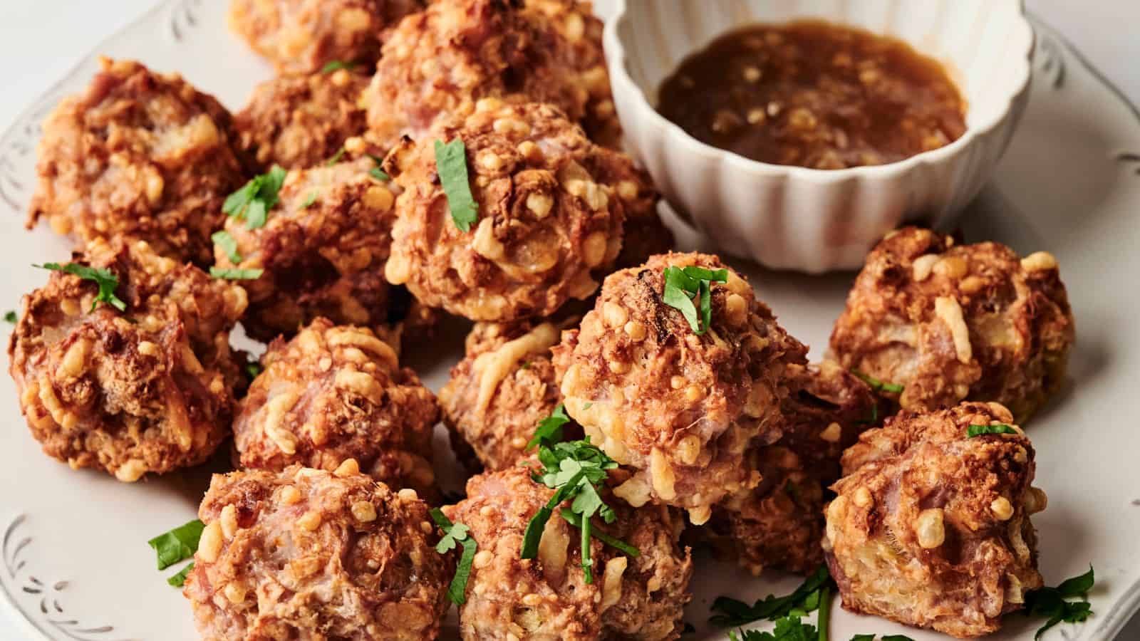 Plate of crispy fried dumplings with chopped herbs, served with a bowl of brown dipping sauce.