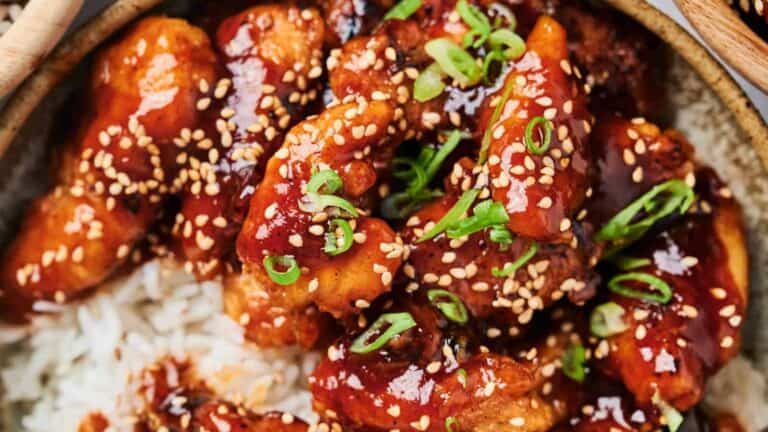 Sesame Chicken with sesame seeds and chopped scallions on a bed of rice.