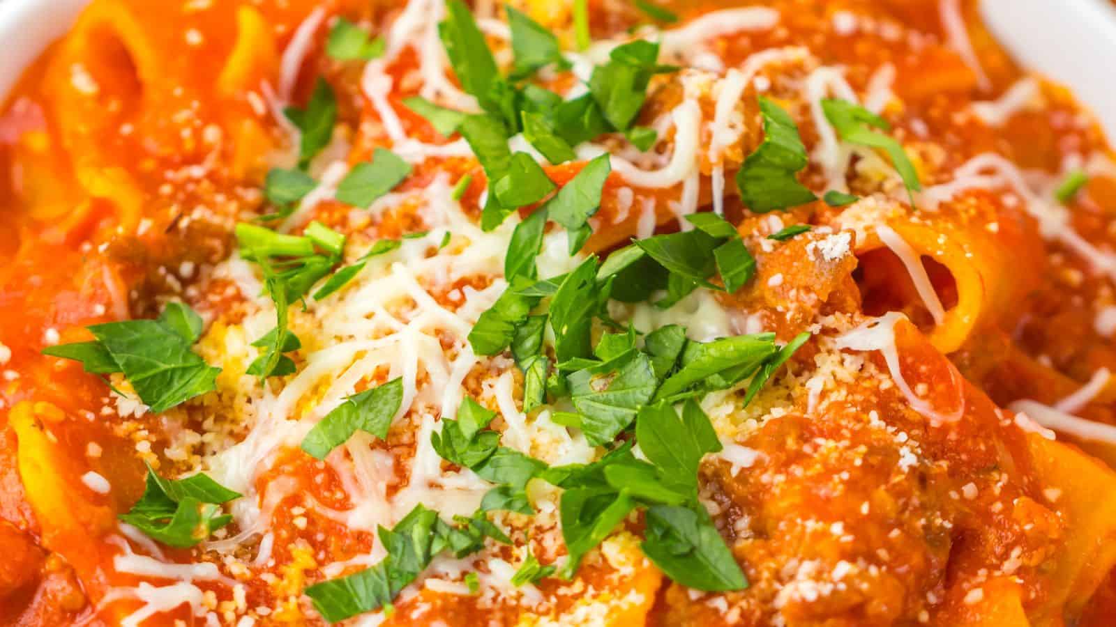 Close-up of a plate of pasta topped with a red tomato-based sauce, grated cheese, and garnished with chopped parsley.