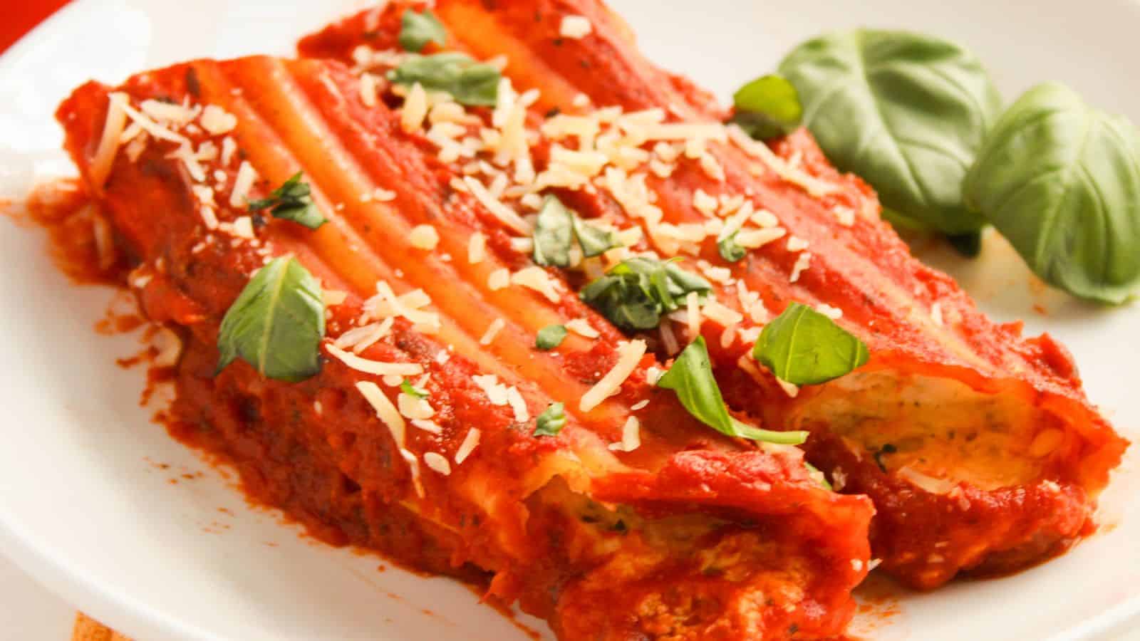 A plate of stuffed cannelloni topped with tomato sauce, grated cheese, and fresh basil.