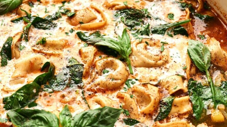 A dish featuring tortellini in creamy tomato sauce, garnished with fresh basil leaves and spinach.