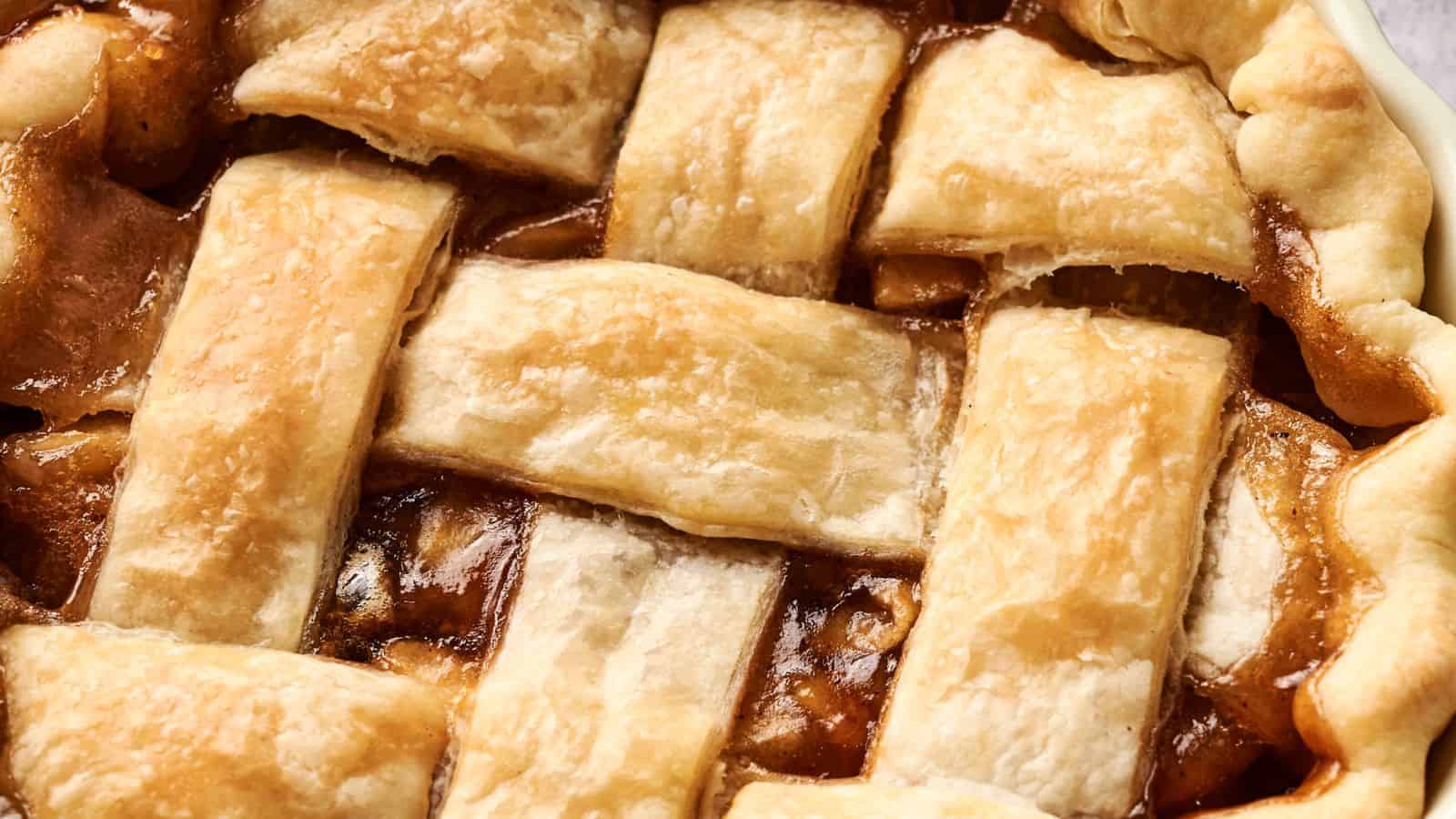 Close-up of a baked pie with a golden brown lattice crust, revealing a caramelized filling underneath.