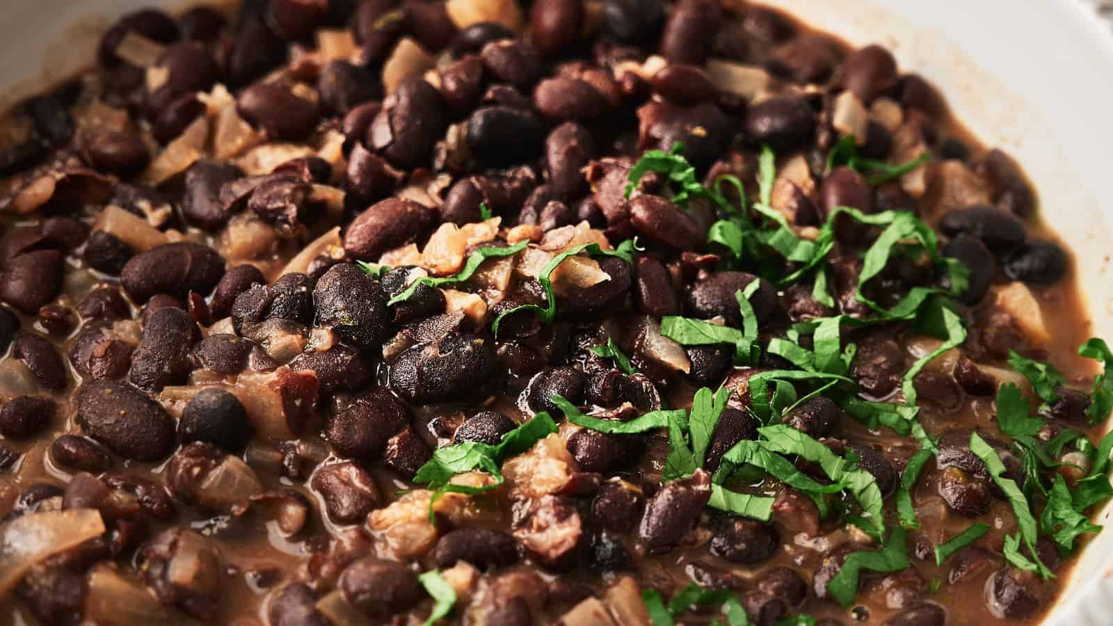 A close-up of a dish featuring black beans mixed with chopped onions and garnished with fresh green herbs.