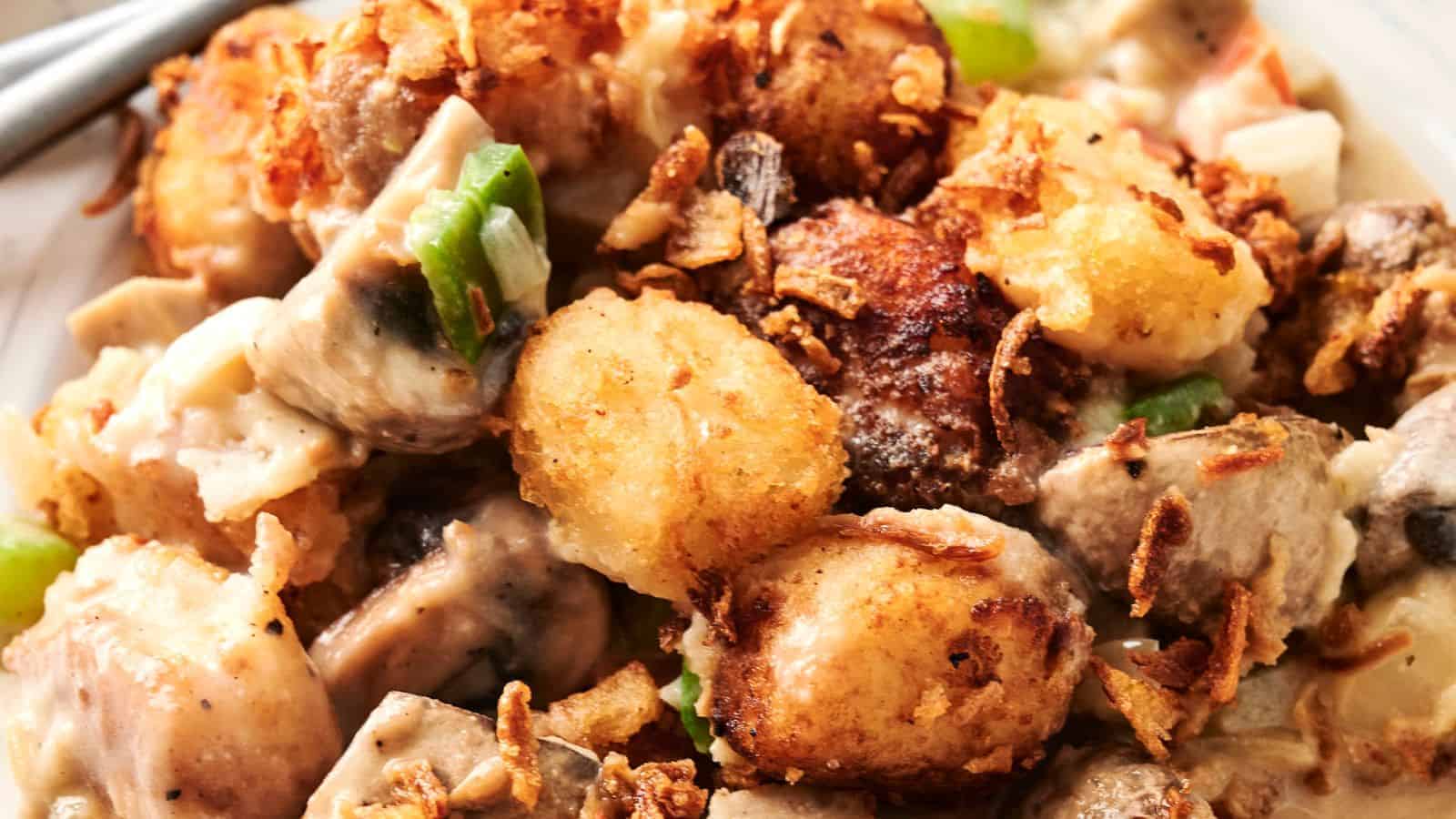 Close-up of a dish with crispy tater tots, green bell peppers, and a creamy sauce, topped with fried onions.