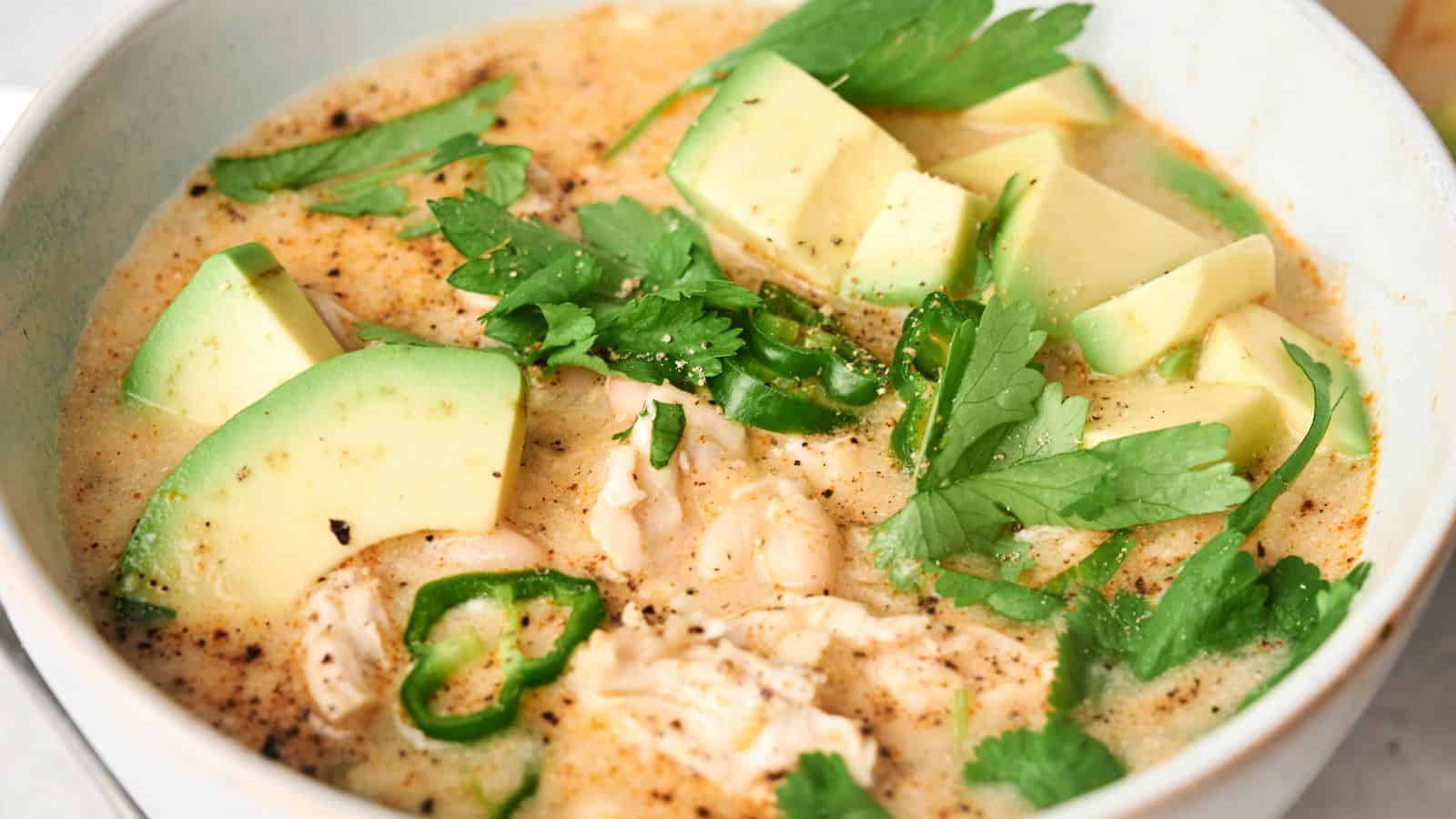 A bowl of creamy White Chicken Chili with chunks of chicken, sliced avocado, green jalapeño peppers, white beans, and fresh cilantro.