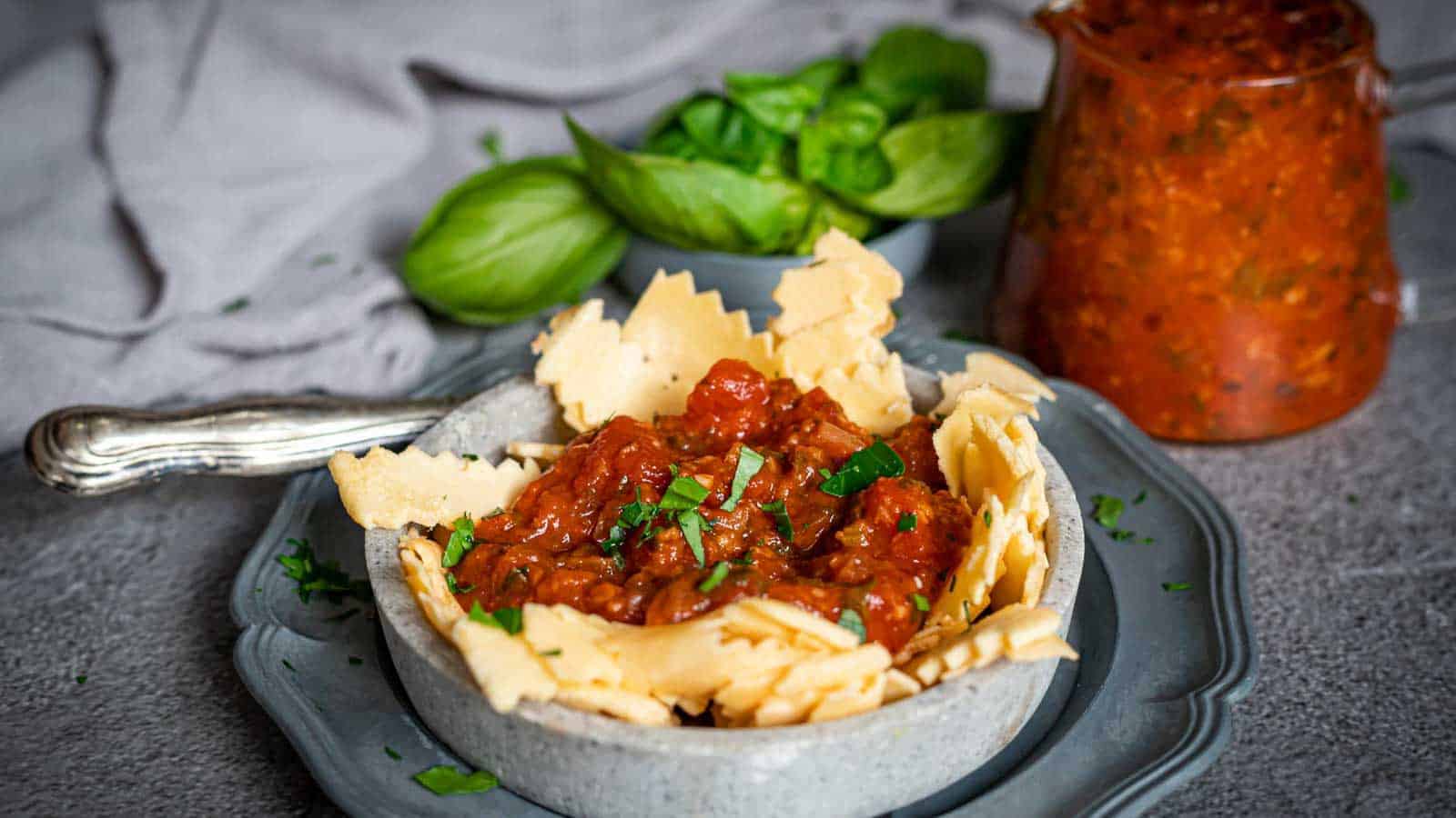 Pasta Marinara inside a grey plate with extra sauce and basil leaves on the side.