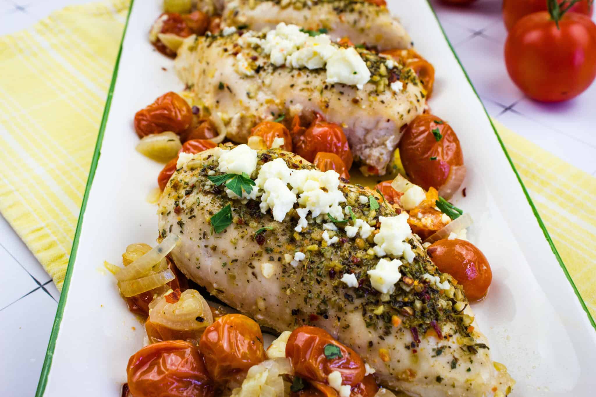 Mediterranean Chicken Bake with herbs, cheese and tomatoes in a platter.