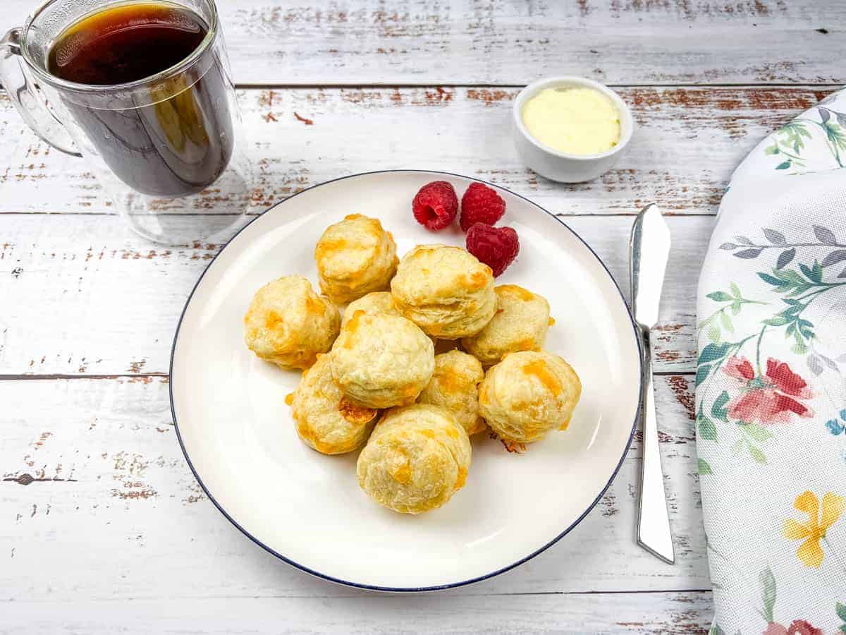 A plate of mini flaky cheese biscuits and a cup of coffee.