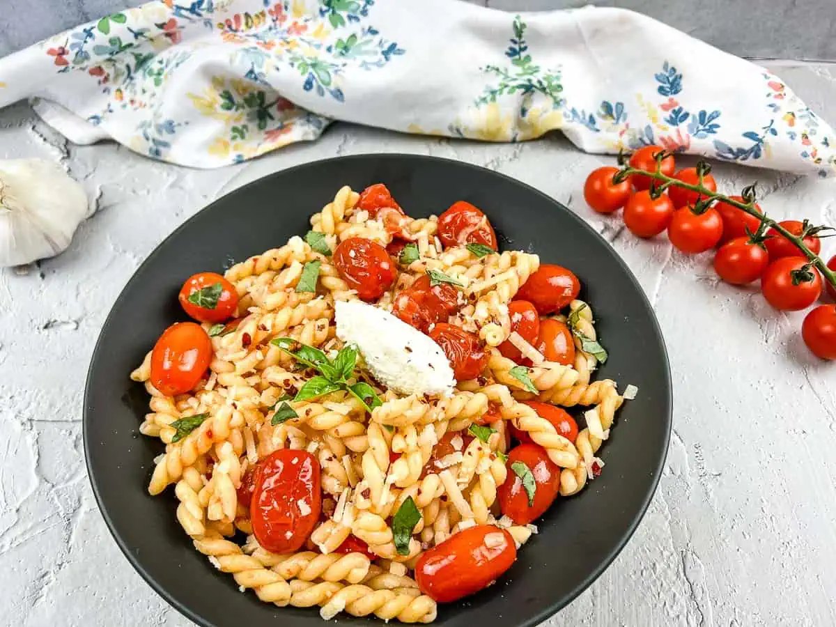 A bowl of Pasta with Fresh Cherry Tomato Sauce, alongside cherry tomatoes and garlic.