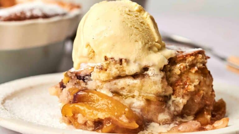 A close-up of a slice of peach cobbler topped with a scoop of vanilla ice cream on a white plate.