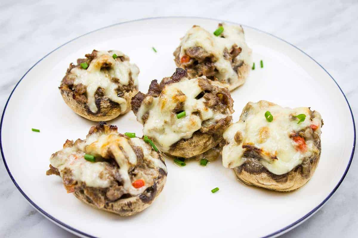 Five stuffed mushrooms on a white plate.