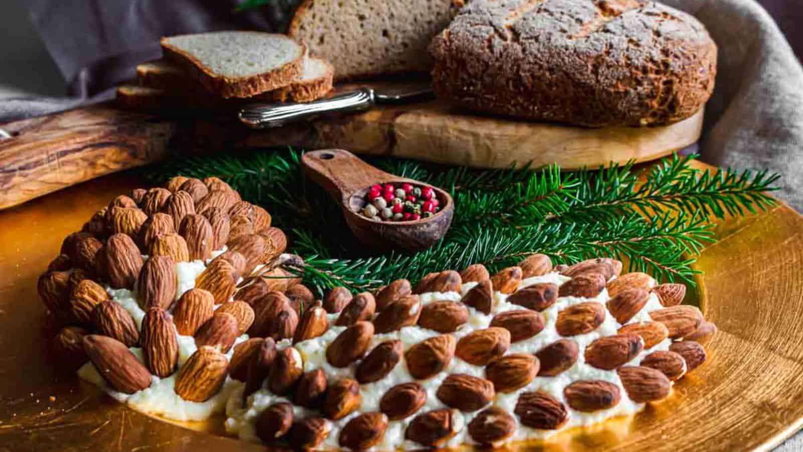 Pine Cone Cheese Ball on a board with bread behind.