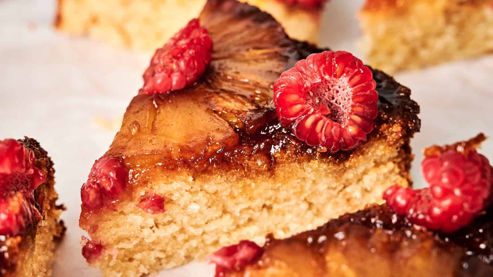 A slice of pineapple cake topped with fresh raspberries on a white surface.