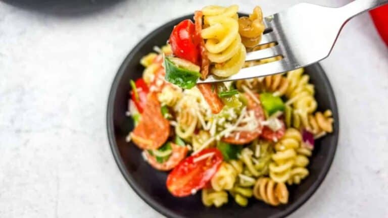 Close-up of a fork holding a colorful bite of Pizza Pasta Salad, served on a black plate.