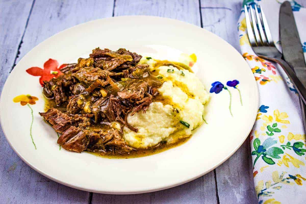 A plate of pot roast with bacon and mashed potatoes with gravy.