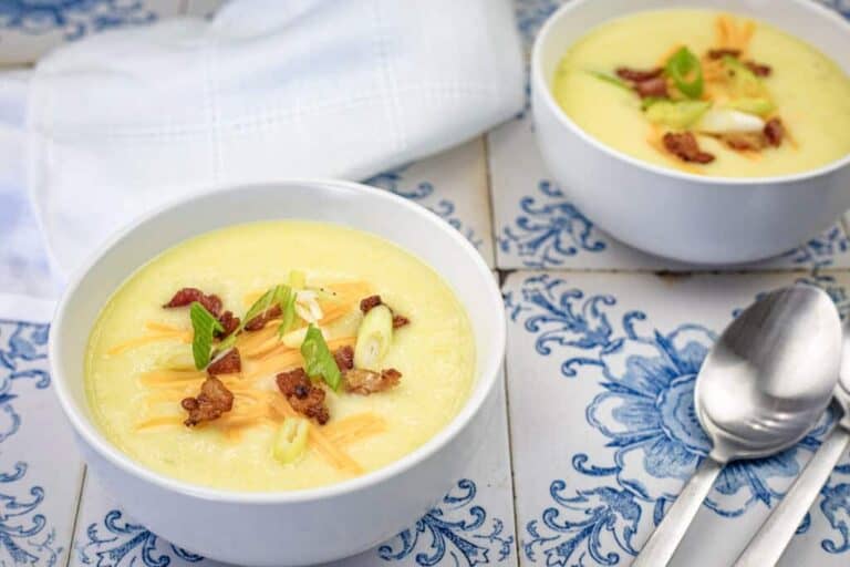 Two bowls of Copycat La Madeleine Country Potato Soup were placed on a marble surface next to two spoons.