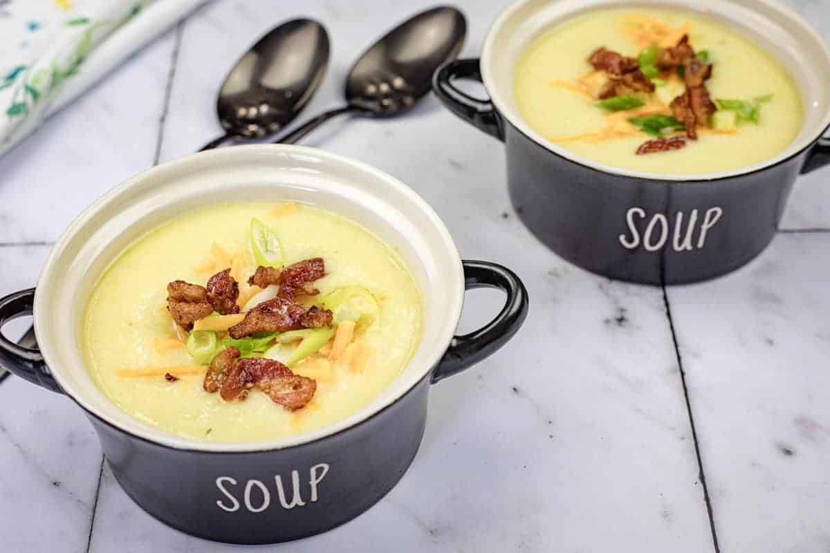 Two bowls of Potato leek soup with two spoons beside.