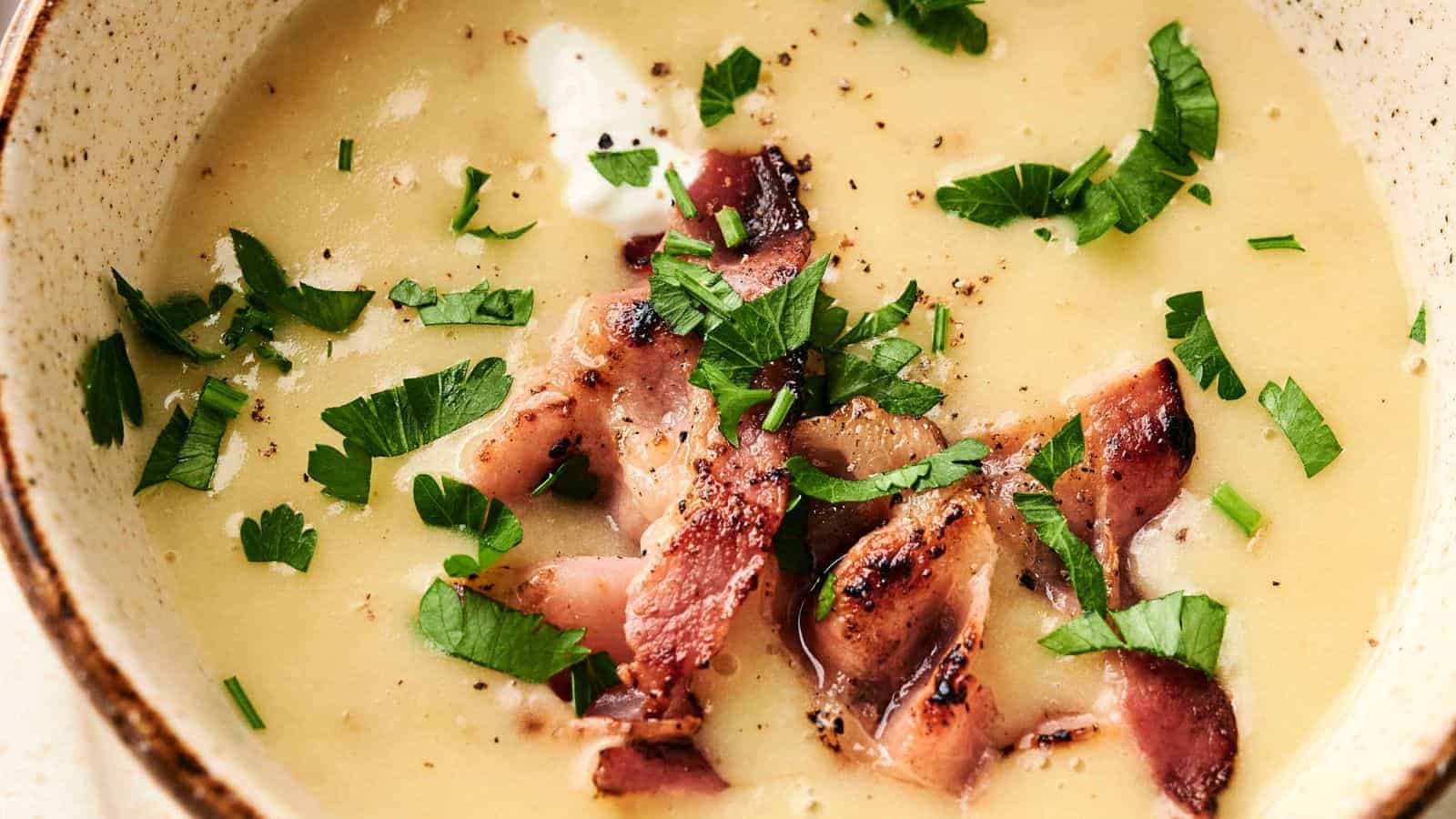 Close-up of a bowl of creamy soup topped with grilled bacon pieces and chopped parsley.