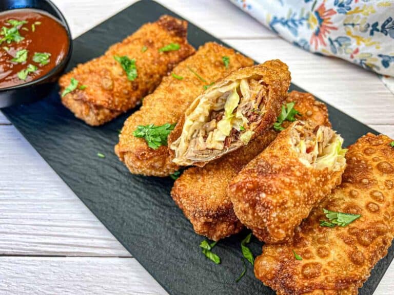 A plate of crispy fried egg rolls is garnished with chopped herbs and a small bowl of dipping sauce.