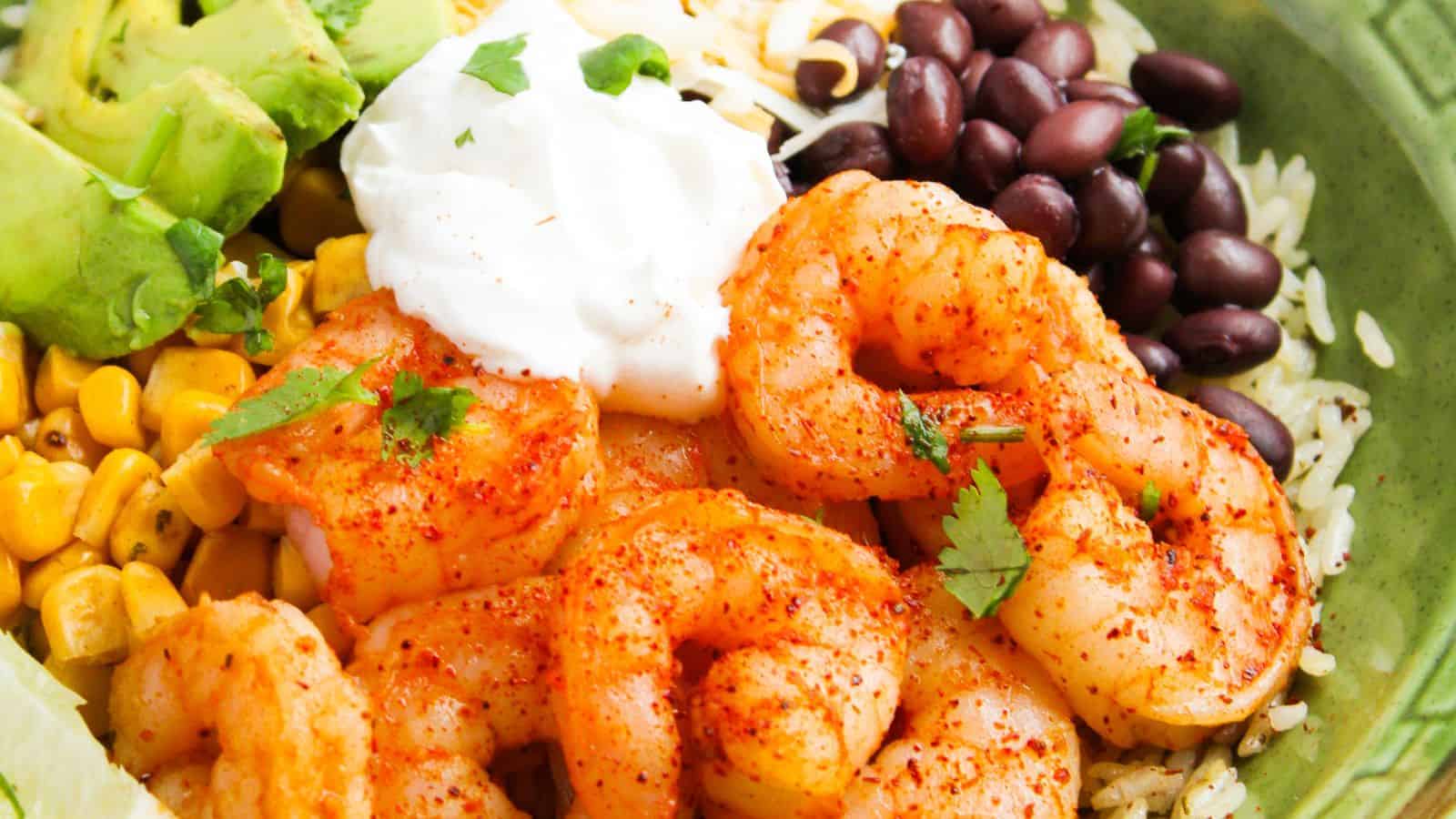 A bowl of seasoned shrimp, avocado, corn, black beans, rice, and a dollop of sour cream, garnished with cilantro.