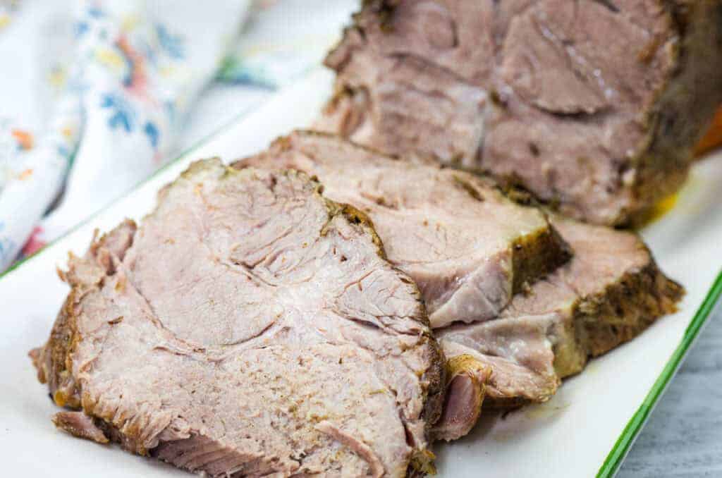 Sliced Herb-Crusted Pork Roast on a rectangular white plate with a floral napkin in the background.