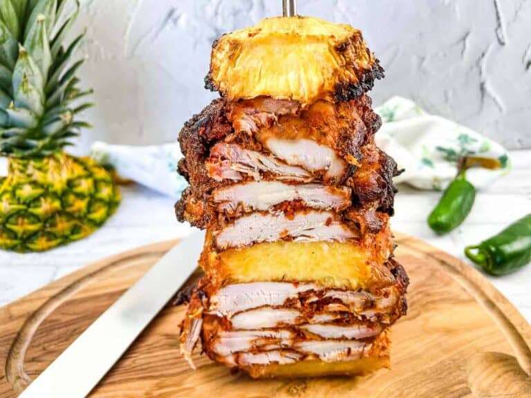 A stack of chicken and pineapple on a vertical skewer on a cutting board.