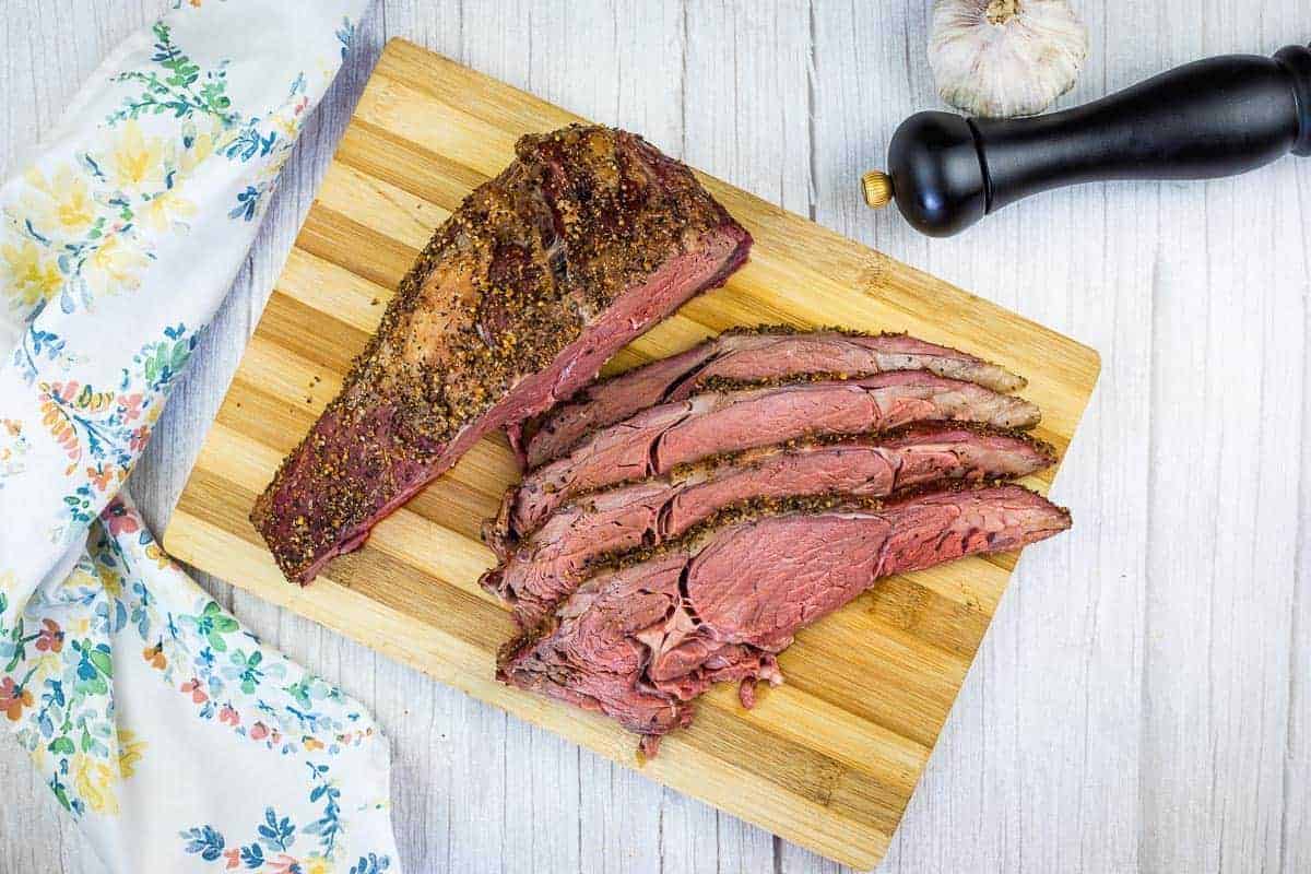 Sliced smoked ribeye beef on a cutting board.