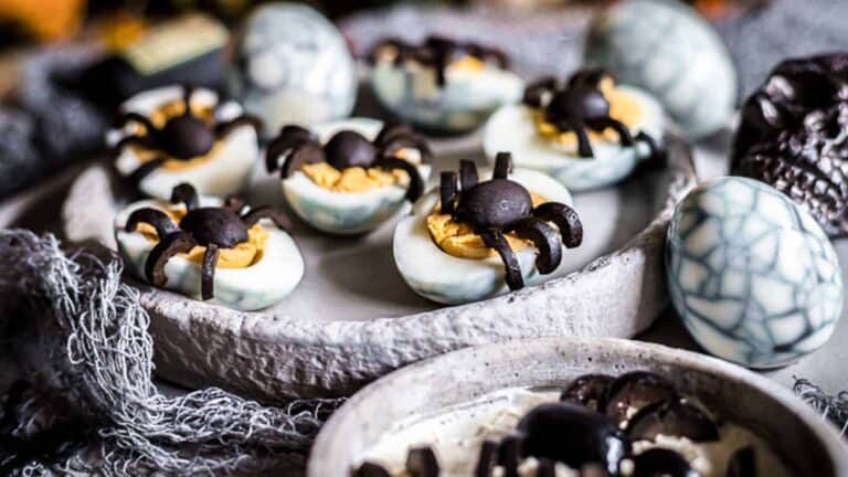 Eggs colored and cut into half with olives designed in the shape of spider on top.