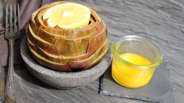 An artichoke in a bowl with lemon slices and a fork.