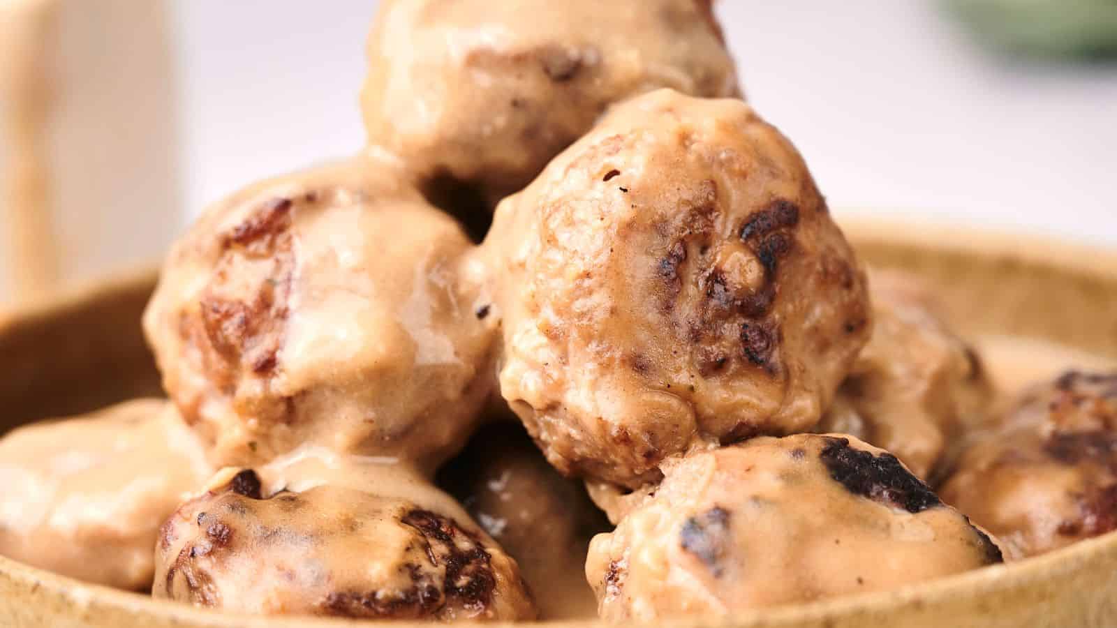 A close-up of Swedish meatballs covered in a creamy sauce, piled in a wooden bowl.