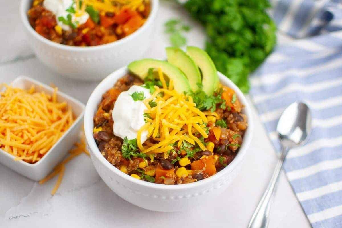 Two bowls of quinoa salad topped with avocado slices, cheese, and sour cream.