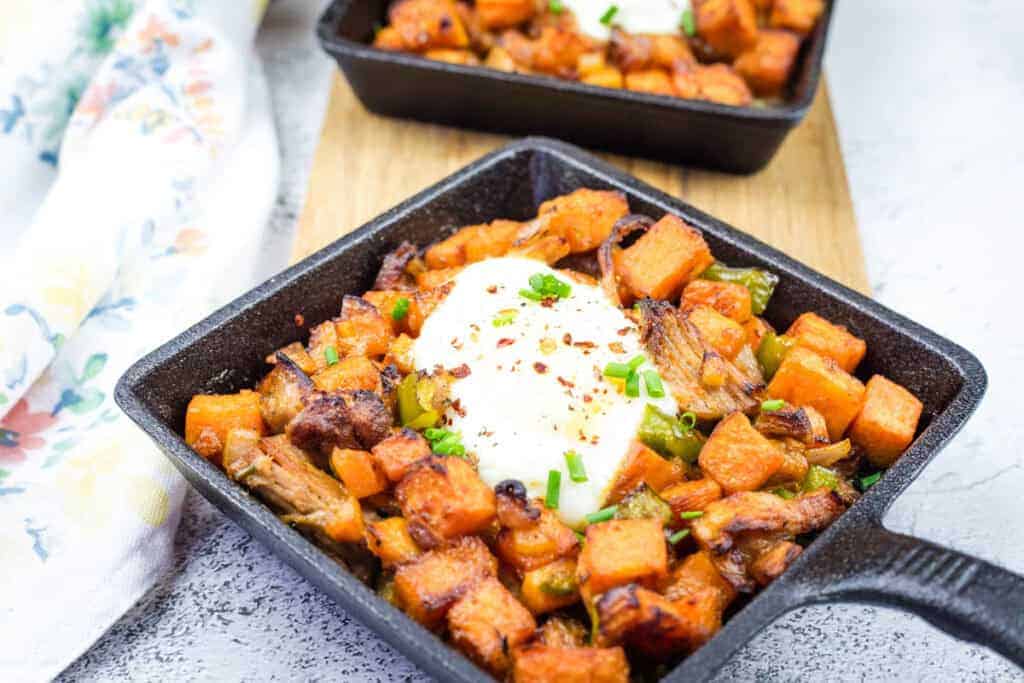 Cast iron skillet with sweet potato hash with pulled pork and garnished with chopped chives.