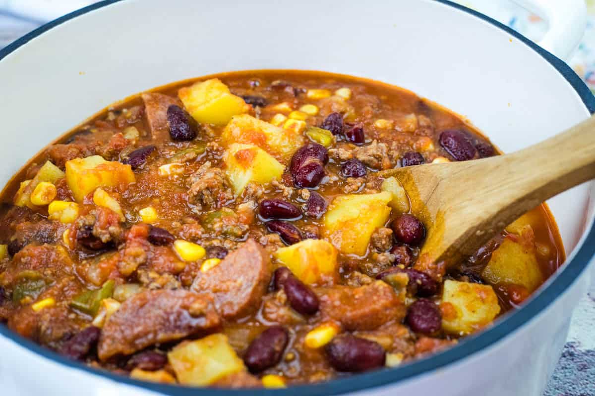 A pot filled with a Texas Cowboy stew is being stirred with a wooden spoon.