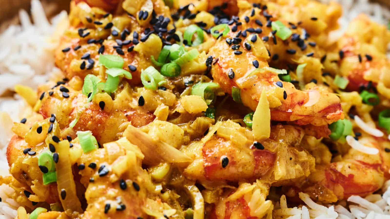 Close-up of a shrimp curry dish with rice, topped with black sesame seeds and chopped green onions.