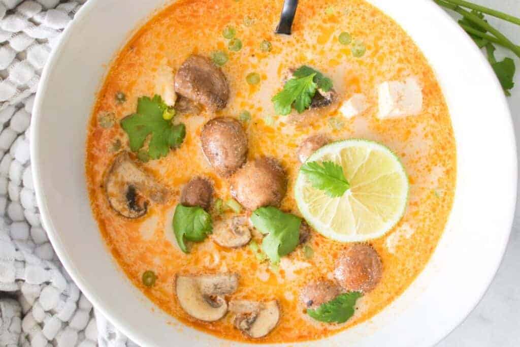 A bowl of Tom Kha Soup with green herbs, and a slice of lime.