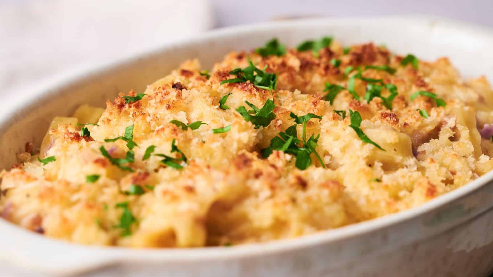 A baking dish filled with golden-brown baked tuna noodle casserole, topped with breadcrumbs and garnished with chopped parsley.